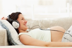 Smiling pregnant woman with headphones lying on couch listening music